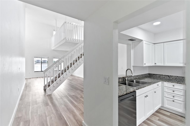 kitchen with light wood-style flooring, dark stone counters, a sink, white cabinetry, and dishwasher