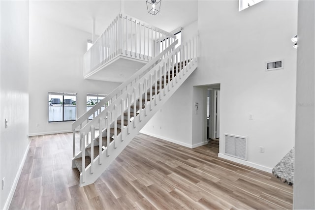 staircase featuring a high ceiling, visible vents, baseboards, and wood finished floors