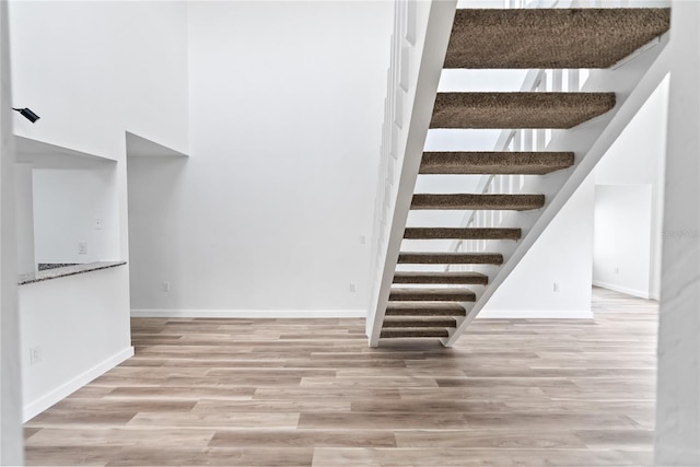 stairs with a high ceiling, wood finished floors, and baseboards