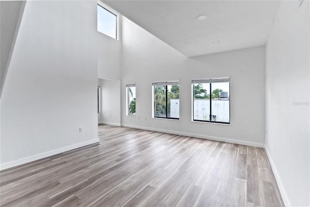 unfurnished living room featuring wood finished floors, a towering ceiling, and baseboards