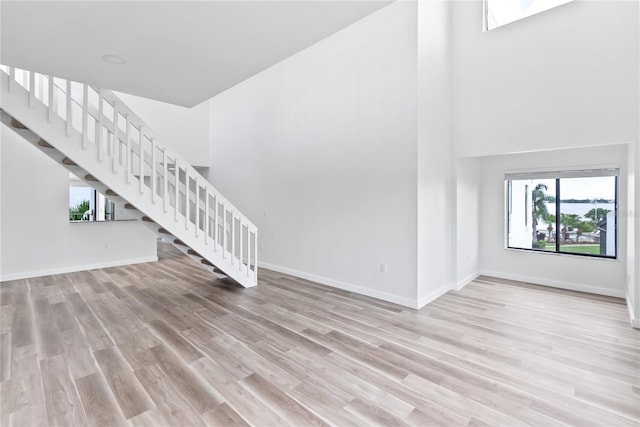 unfurnished living room with stairway, wood finished floors, a towering ceiling, and baseboards