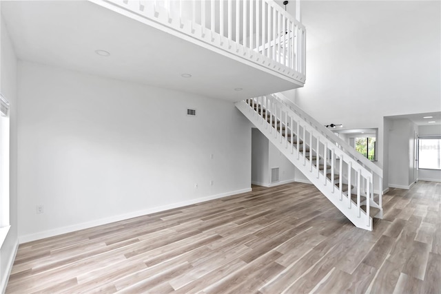 unfurnished living room featuring baseboards, visible vents, stairway, and wood finished floors