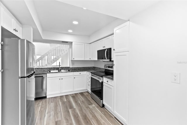 kitchen featuring light wood-style flooring, stainless steel appliances, white cabinetry, a sink, and recessed lighting