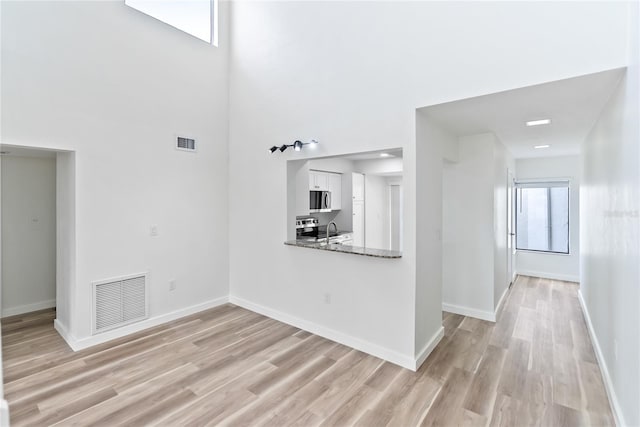 unfurnished living room with light wood-style flooring, a sink, visible vents, and baseboards