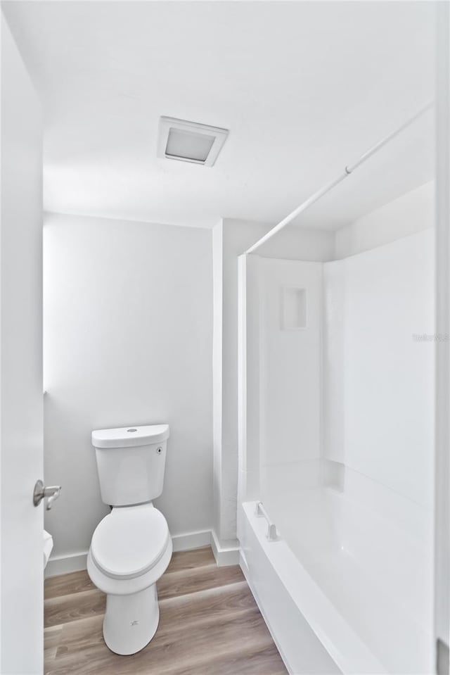 bathroom with baseboards, shower / bathing tub combination, toilet, and wood finished floors