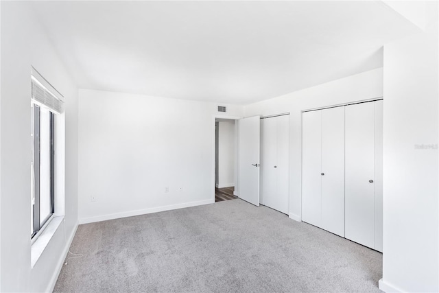 unfurnished bedroom with multiple closets, carpet, multiple windows, and baseboards