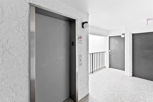 hallway with elevator and a textured wall