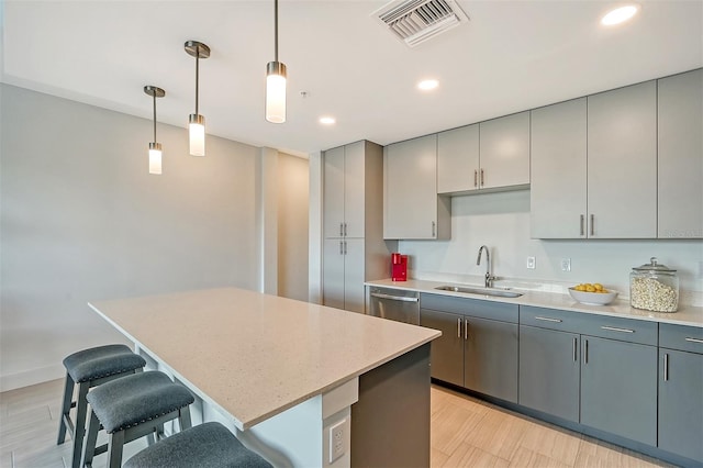 kitchen with gray cabinets, stainless steel dishwasher, hanging light fixtures, a center island, and light stone counters