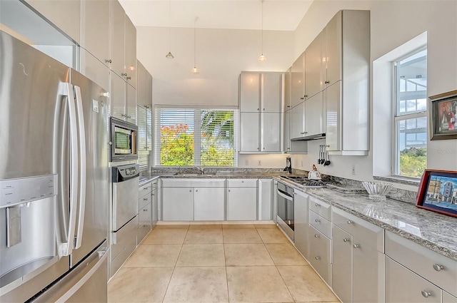 kitchen with light tile patterned floors, a wealth of natural light, light stone countertops, and appliances with stainless steel finishes