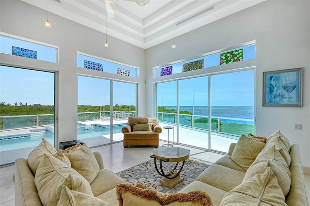 tiled living room featuring a water view, a healthy amount of sunlight, a high ceiling, and a tray ceiling