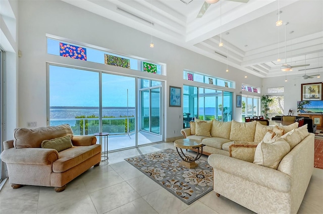 living room with a high ceiling, a water view, ceiling fan, tile patterned floors, and a raised ceiling