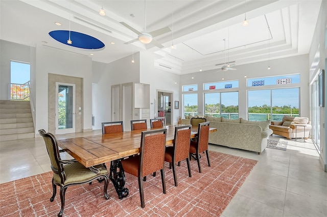 tiled dining space with ceiling fan, a raised ceiling, and a towering ceiling