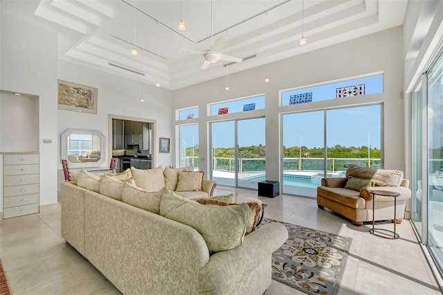 living room featuring light tile patterned flooring, a high ceiling, ceiling fan, and a raised ceiling