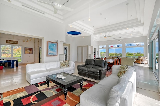 tiled living room featuring a tray ceiling, a high ceiling, and ceiling fan