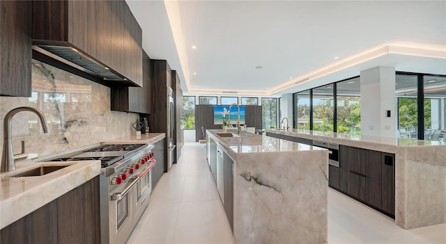 kitchen featuring sink, light stone counters, light tile patterned flooring, an island with sink, and decorative backsplash