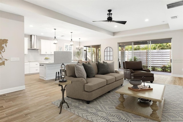 living room with a raised ceiling and ceiling fan with notable chandelier