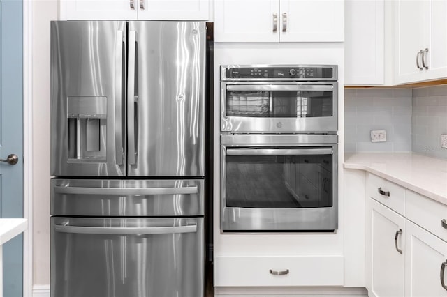 kitchen with tasteful backsplash, light stone countertops, white cabinets, and appliances with stainless steel finishes