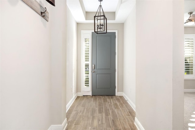 entryway featuring a tray ceiling, light hardwood / wood-style flooring, and a chandelier