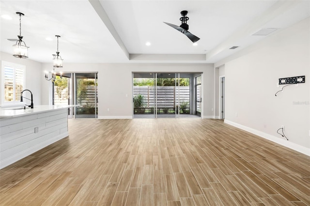 unfurnished living room featuring ceiling fan with notable chandelier, a healthy amount of sunlight, light wood-type flooring, and sink