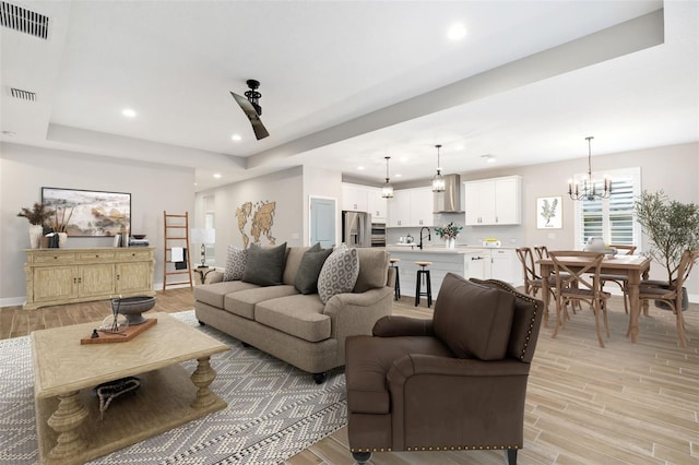 living room with a raised ceiling, light wood-type flooring, sink, and an inviting chandelier