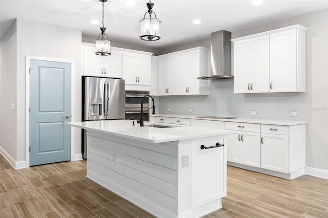 kitchen with pendant lighting, white cabinetry, wall chimney exhaust hood, and an island with sink