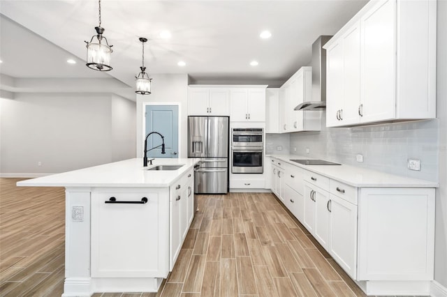 kitchen with white cabinets, sink, hanging light fixtures, wall chimney exhaust hood, and an island with sink