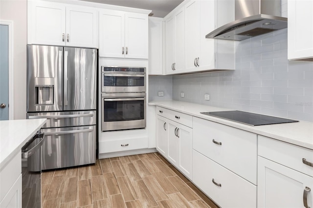 kitchen featuring decorative backsplash, white cabinets, wall chimney range hood, and appliances with stainless steel finishes