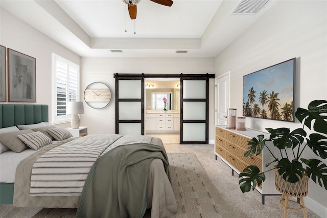 carpeted bedroom with ensuite bathroom, a barn door, ceiling fan, and a tray ceiling