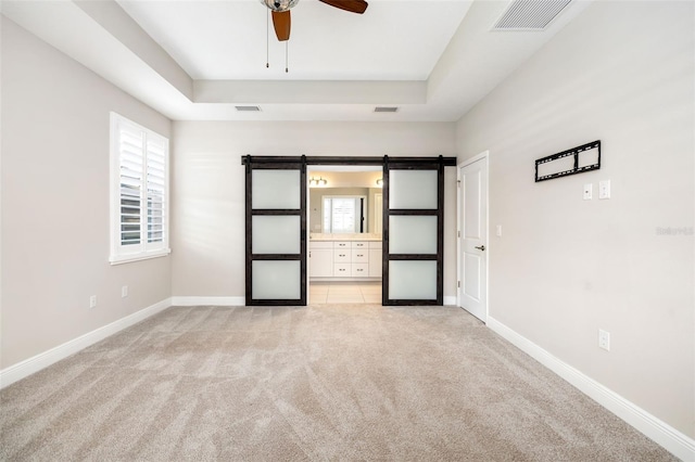 unfurnished bedroom with ceiling fan, a barn door, light carpet, and ensuite bath