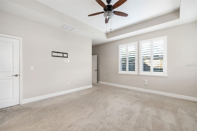 unfurnished room with a raised ceiling, ceiling fan, and light colored carpet