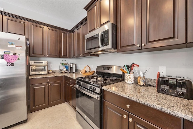 kitchen featuring appliances with stainless steel finishes, a textured ceiling, light tile patterned floors, and dark brown cabinets