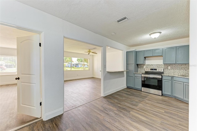 kitchen with backsplash, stainless steel range with electric stovetop, a textured ceiling, ceiling fan, and hardwood / wood-style floors