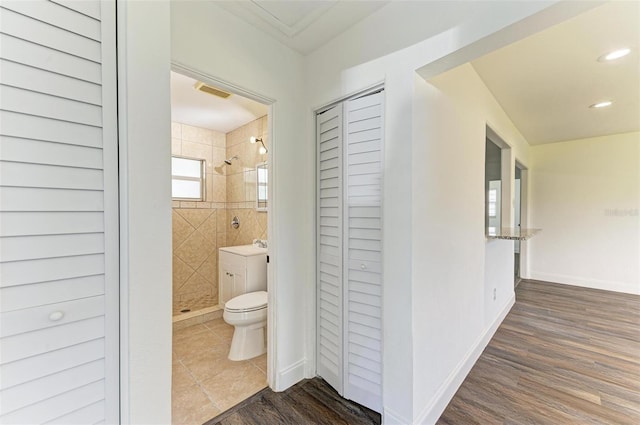 bathroom with a tile shower, vanity, wood-type flooring, and toilet