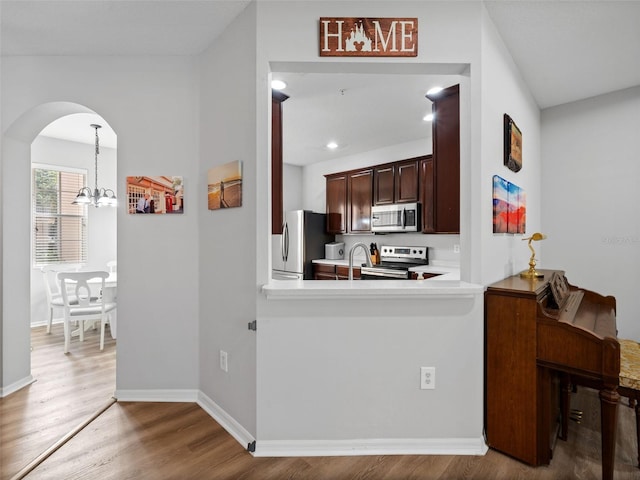 kitchen featuring hardwood / wood-style floors, stainless steel appliances, a notable chandelier, dark brown cabinets, and pendant lighting