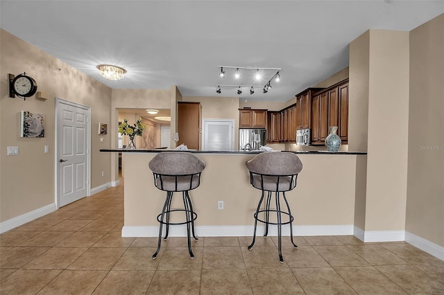 kitchen with a kitchen breakfast bar, light tile patterned floors, kitchen peninsula, and appliances with stainless steel finishes