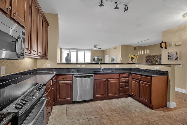 kitchen featuring sink, dark stone countertops, light tile patterned flooring, kitchen peninsula, and stainless steel appliances