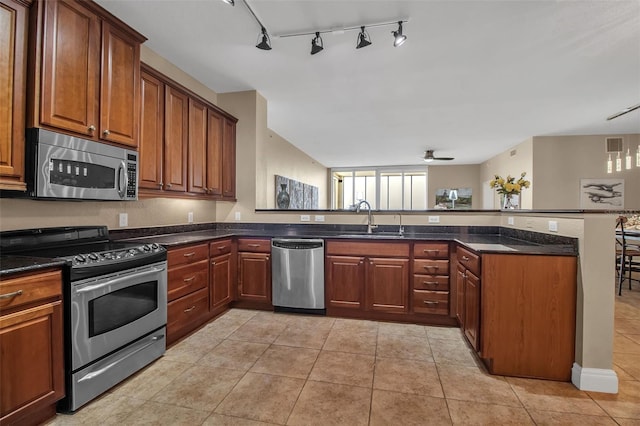 kitchen with kitchen peninsula, appliances with stainless steel finishes, ceiling fan, sink, and dark stone countertops