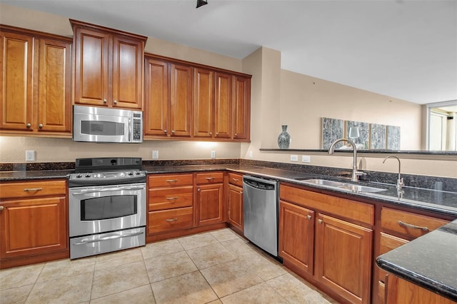 kitchen with light tile patterned flooring, appliances with stainless steel finishes, dark stone counters, and sink