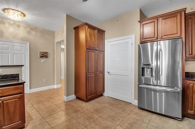 kitchen with stainless steel refrigerator with ice dispenser, an inviting chandelier, light tile patterned floors, and dark stone countertops