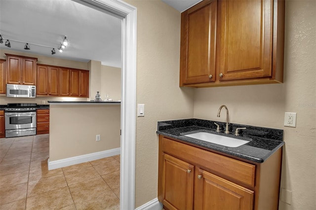 kitchen featuring rail lighting, sink, dark stone countertops, light tile patterned floors, and appliances with stainless steel finishes