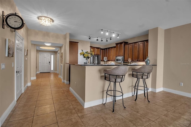 kitchen featuring kitchen peninsula, appliances with stainless steel finishes, a breakfast bar, light tile patterned floors, and a chandelier