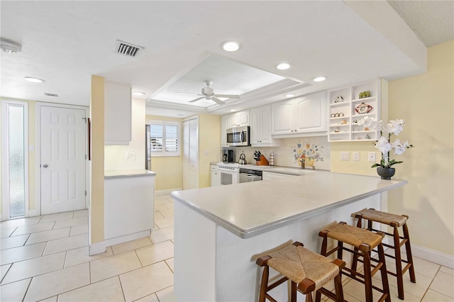 kitchen with visible vents, stainless steel microwave, a breakfast bar area, light countertops, and white cabinetry