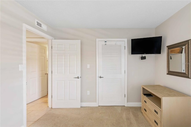 unfurnished bedroom featuring a closet, visible vents, light carpet, a textured ceiling, and baseboards