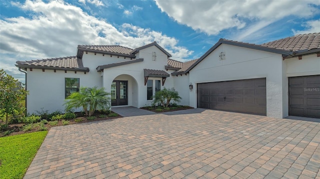 mediterranean / spanish house with decorative driveway, a tile roof, and an attached garage