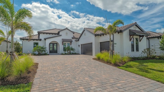 mediterranean / spanish-style house featuring a tile roof, an attached garage, decorative driveway, french doors, and stucco siding