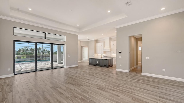 unfurnished living room featuring a raised ceiling, visible vents, a sink, and light wood finished floors