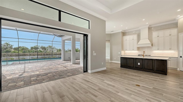 kitchen with light wood finished floors, decorative backsplash, light countertops, premium range hood, and white cabinetry