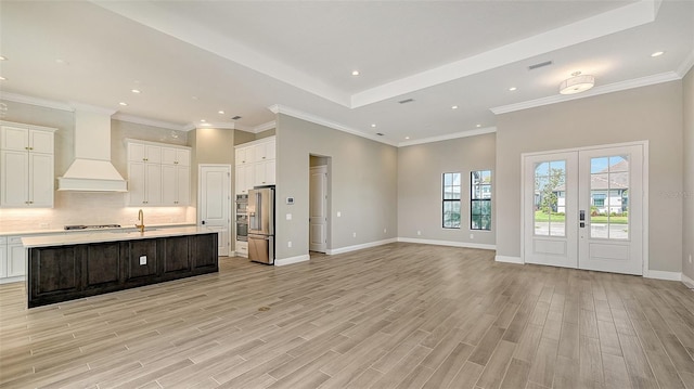 kitchen with open floor plan, light countertops, light wood finished floors, tasteful backsplash, and custom range hood