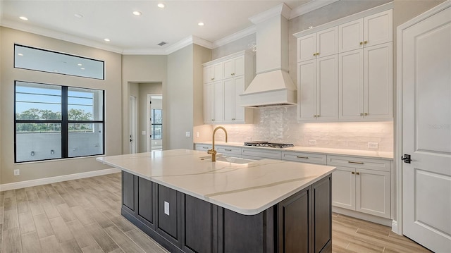 kitchen featuring crown molding, stainless steel gas cooktop, backsplash, white cabinets, and premium range hood