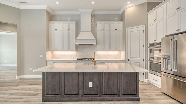 kitchen featuring light wood finished floors, white cabinets, an island with sink, custom exhaust hood, and stainless steel appliances